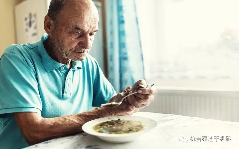 一位患有帕金森病的老人用手握住他的手臂，试图喝汤